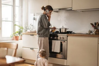 A mother cooking while her toddler plays on the kitchen floor